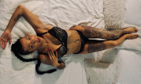 Mulher morena com tatuagens e piercings deitada na cama a ilustrar o que é estigmatofilia.